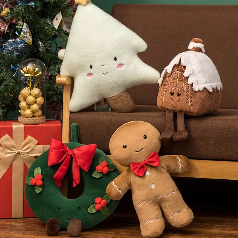 Kawaii plush toys including a gingerbread man, wreath, and tree on a couch with a Christmas tree and gift box in the background.