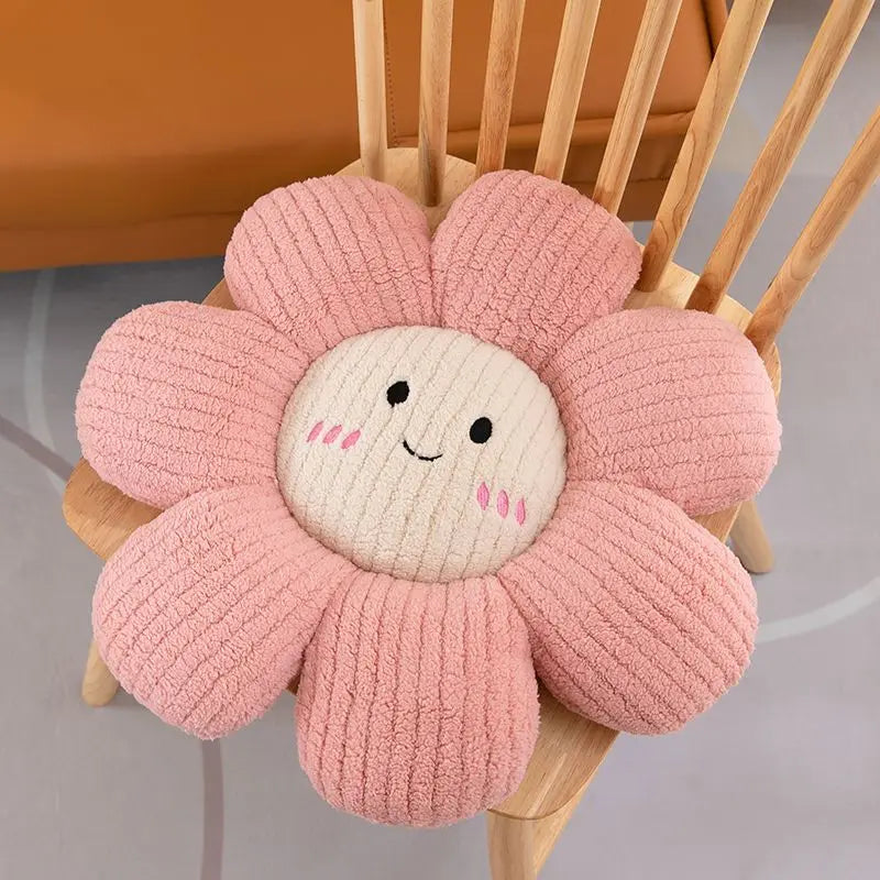 Pink flower-shaped kawaii cushion with a smiling face on a wooden chair.