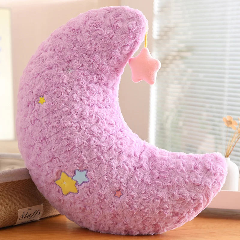 Pink crescent moon-shaped kawaii plush toy with star decorations on a wooden surface.