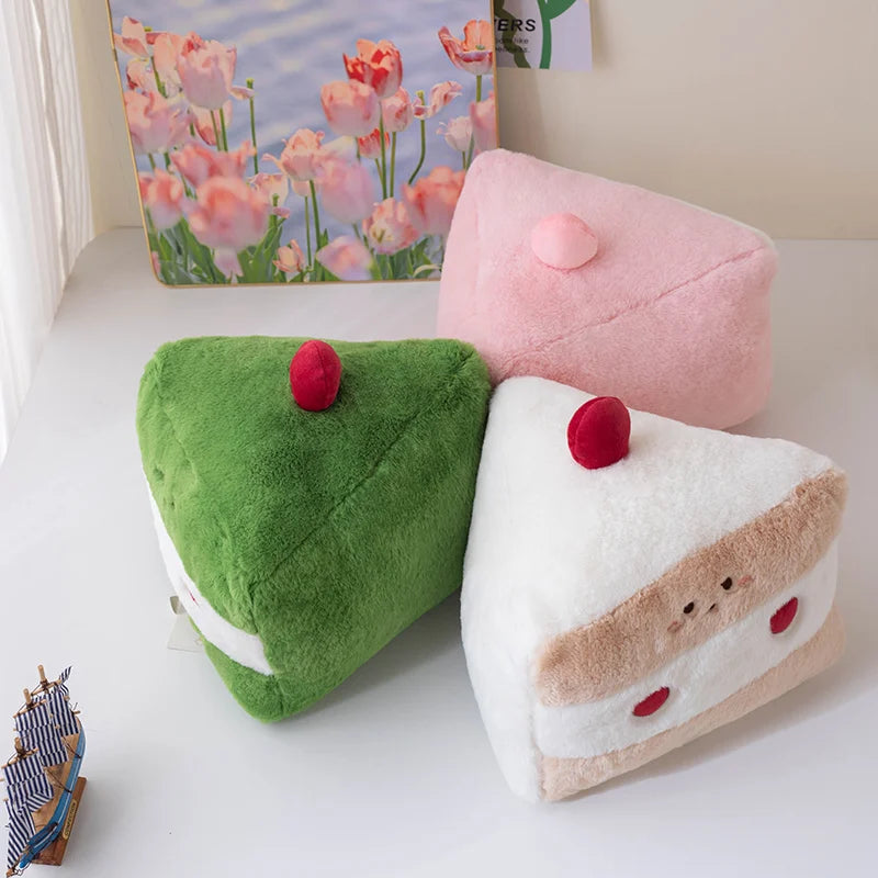 Three colorful cake-shaped plush kawaii toys on a white surface with a floral picture in the background.