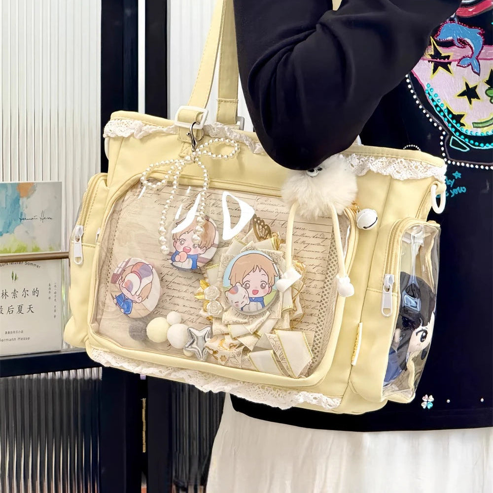 Beige handbag with Kawaii cartoon character charms held by a person wearing a black outfit with colorful design.