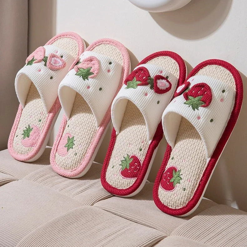Pair of white slippers with pink strawberry kawaii design on a beige surface.