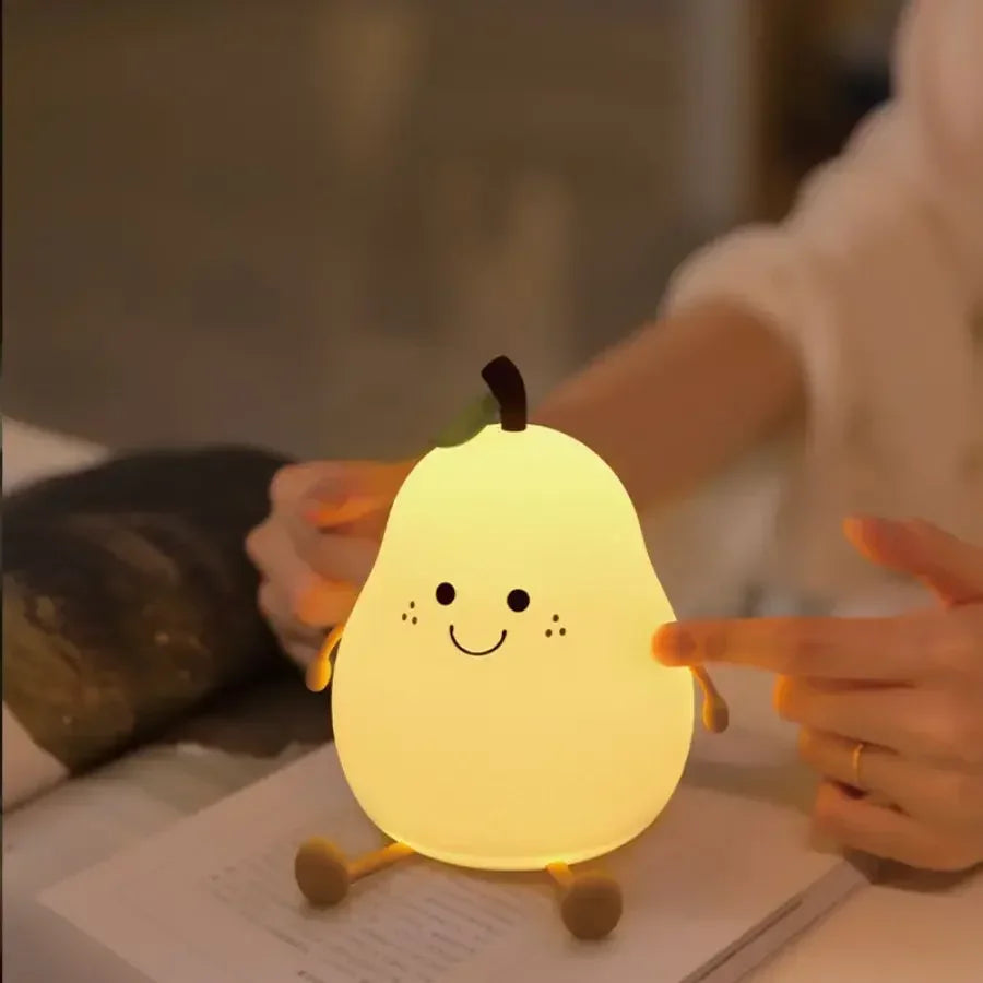 Pear-shaped kawaii night light with a smiling face held by a person on a table.
