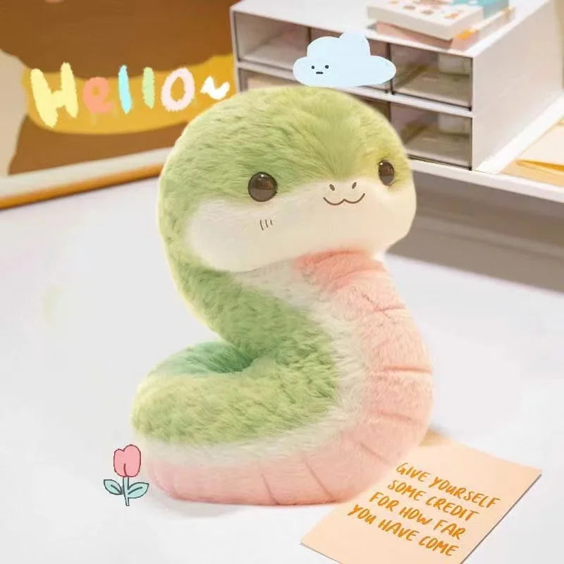 Plush kawaii toy snake with a 'Hello' sign and motivational note on a light background