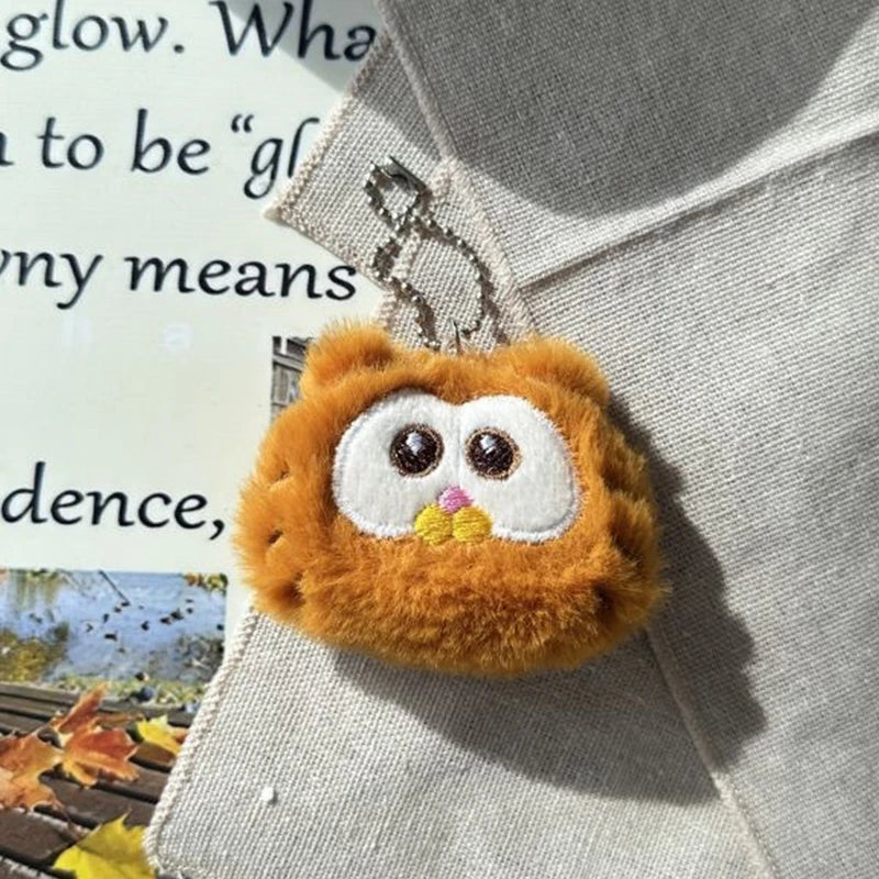 Plush kawaii owl keychain on a textured surface with text in the background