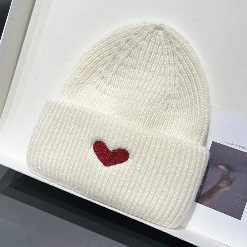 White Kawaii knit beanie with a red heart on a white surface