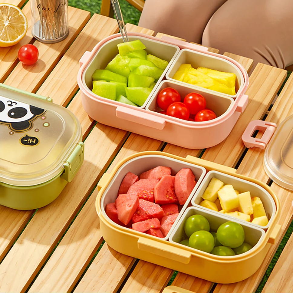 Two kawaii bento boxes with compartments of fruits on a wooden table outdoors.