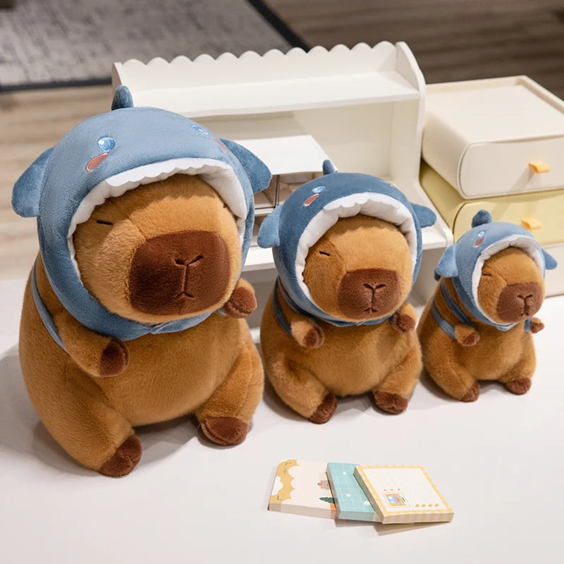 Three kawaii plush toys resembling bears wearing blue shark costumes on a light surface.