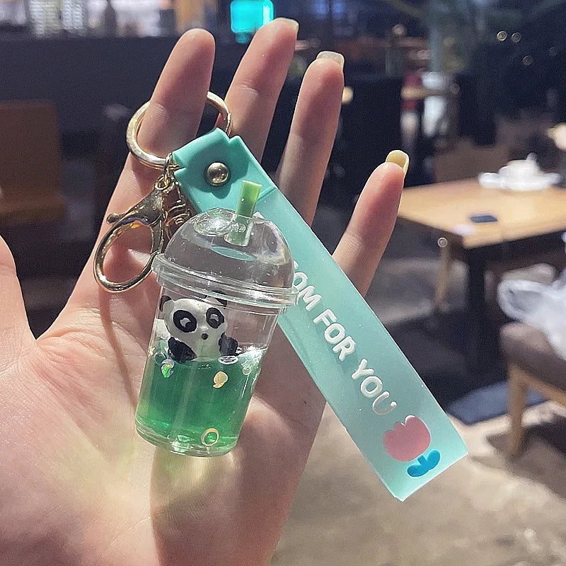 Keychain with kawaii panda design and green liquid held by a hand in an indoor setting.