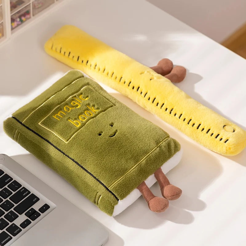 Kawaii plush toy shaped like a book and ruler on a desk next to a laptop