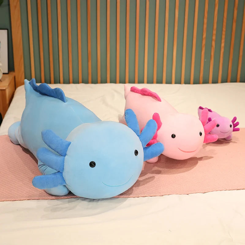 Two axolotl plush kawaii toys, one blue and one pink, on a bed with a striped headboard.