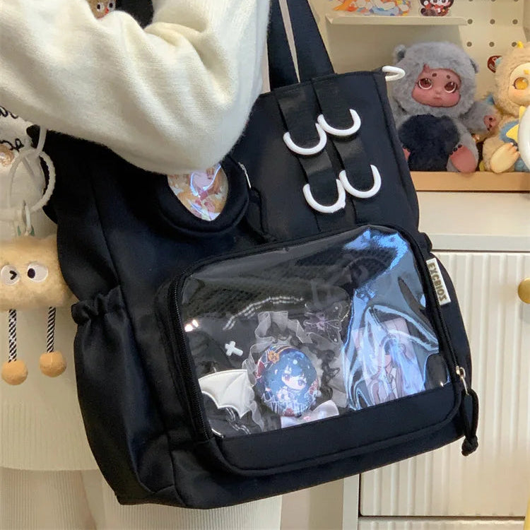 Black Kawaii backpack with clear front pocket featuring cartoon designs, held by a person in a white coat.