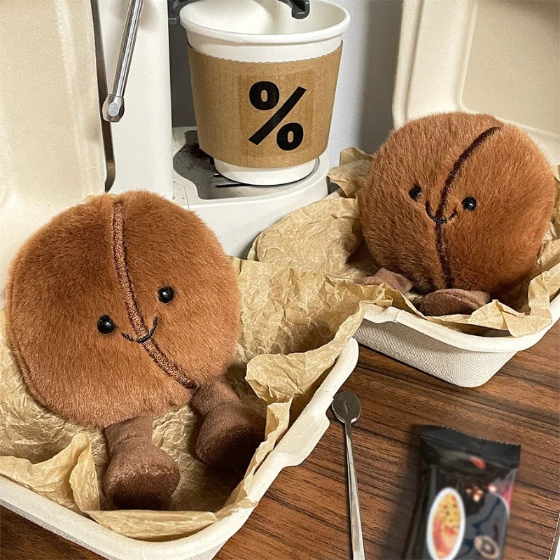 Two kawaii plush cookies in a container with a coffee cup and spoon on a wooden surface.