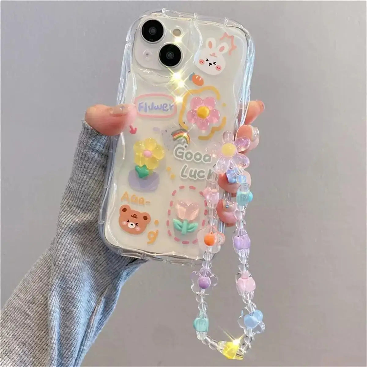 Phone case with kawaii decorative elements and a string attached, held by a hand against a gray background.