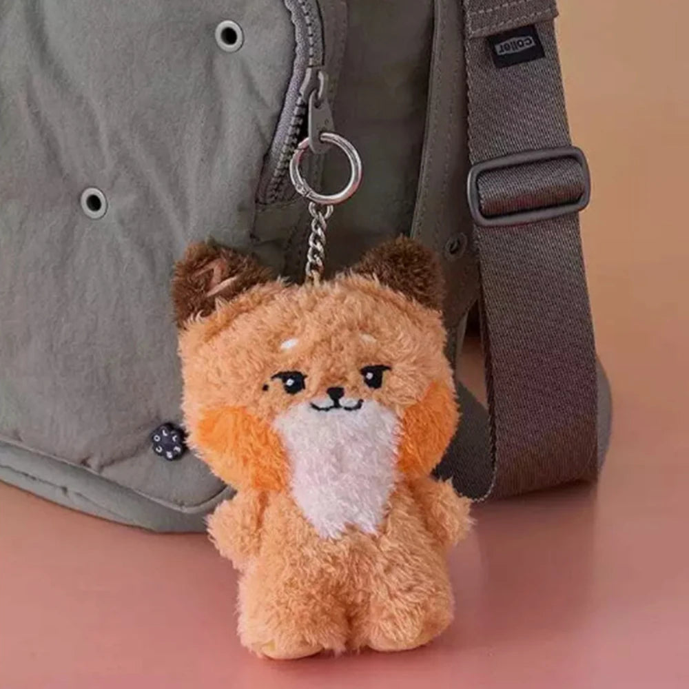 Plush kawaii fox keychain attached to a gray bag on a pink surface
