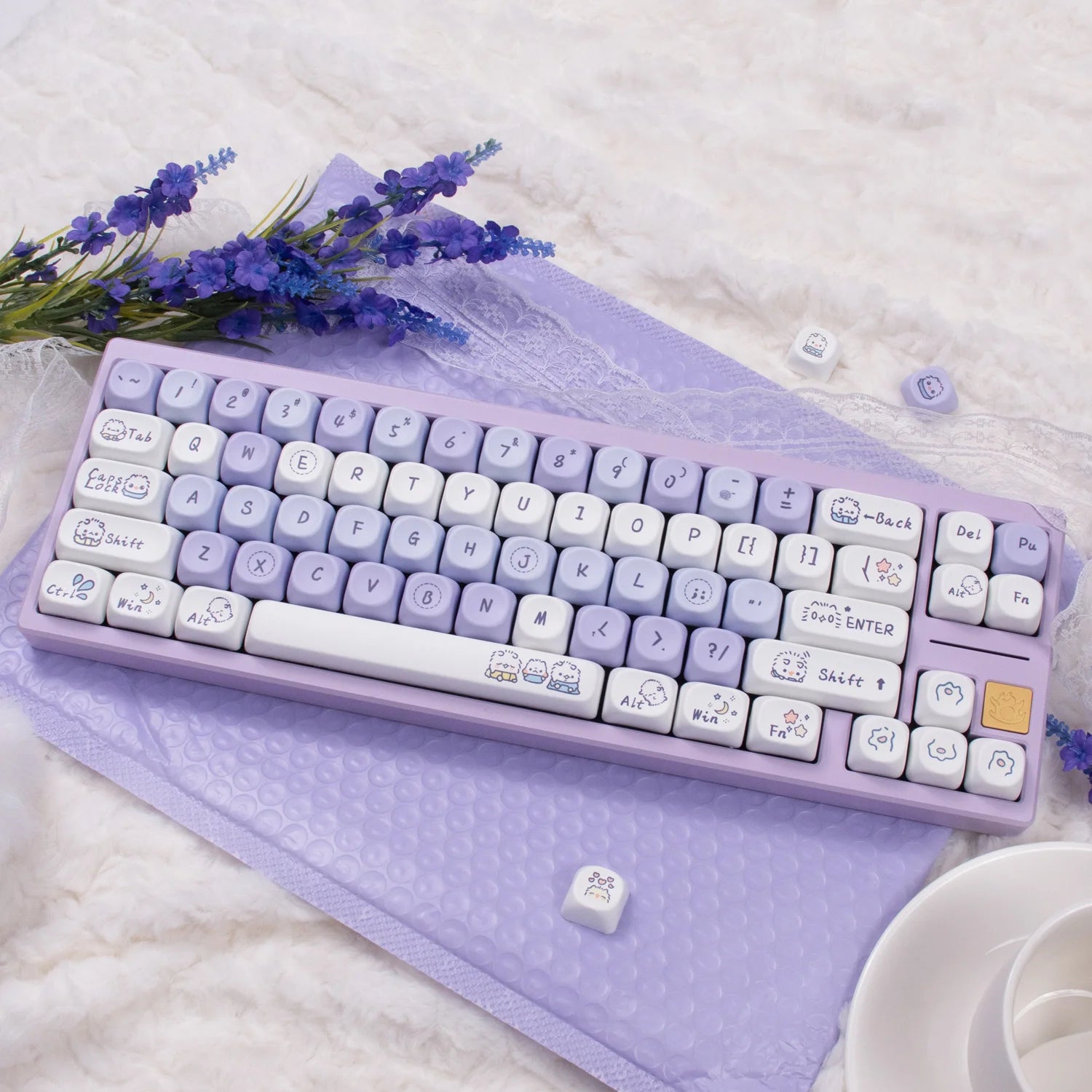 Purple Kawaii keyboard with cute keycaps on a matching mat, surrounded by lavender flowers.