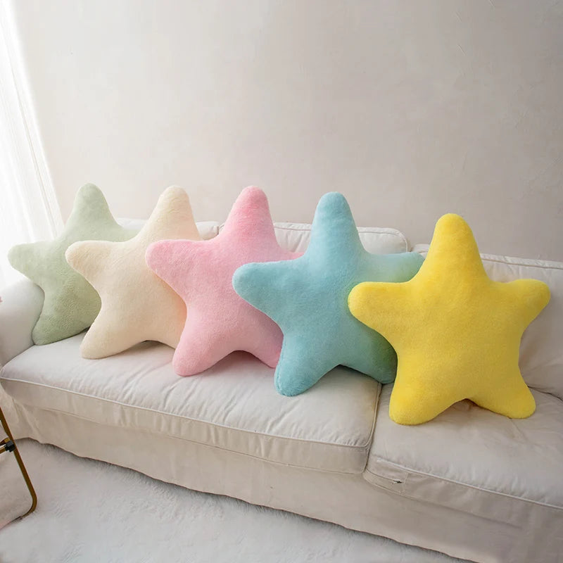 Five colorful star-shaped kawaii cushions on a beige sofa against a white wall.
