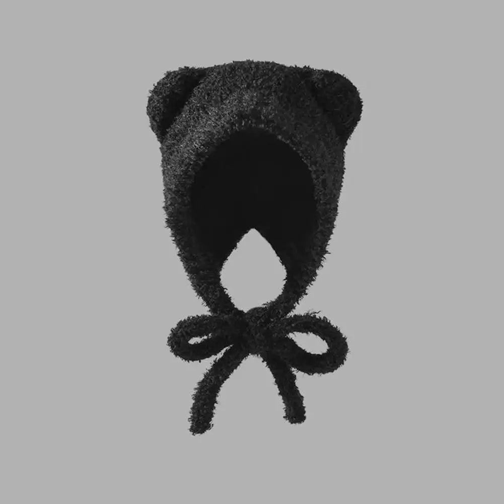 Black fuzzy Kawaii baby bonnet with a bow on a gray background