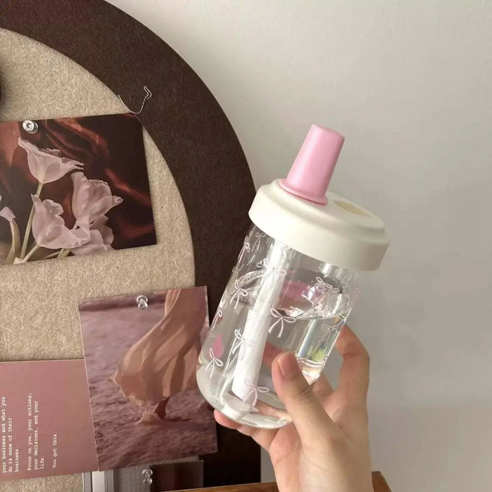 Clear Kawaii bottle with pink and white cap held by a hand against a neutral background