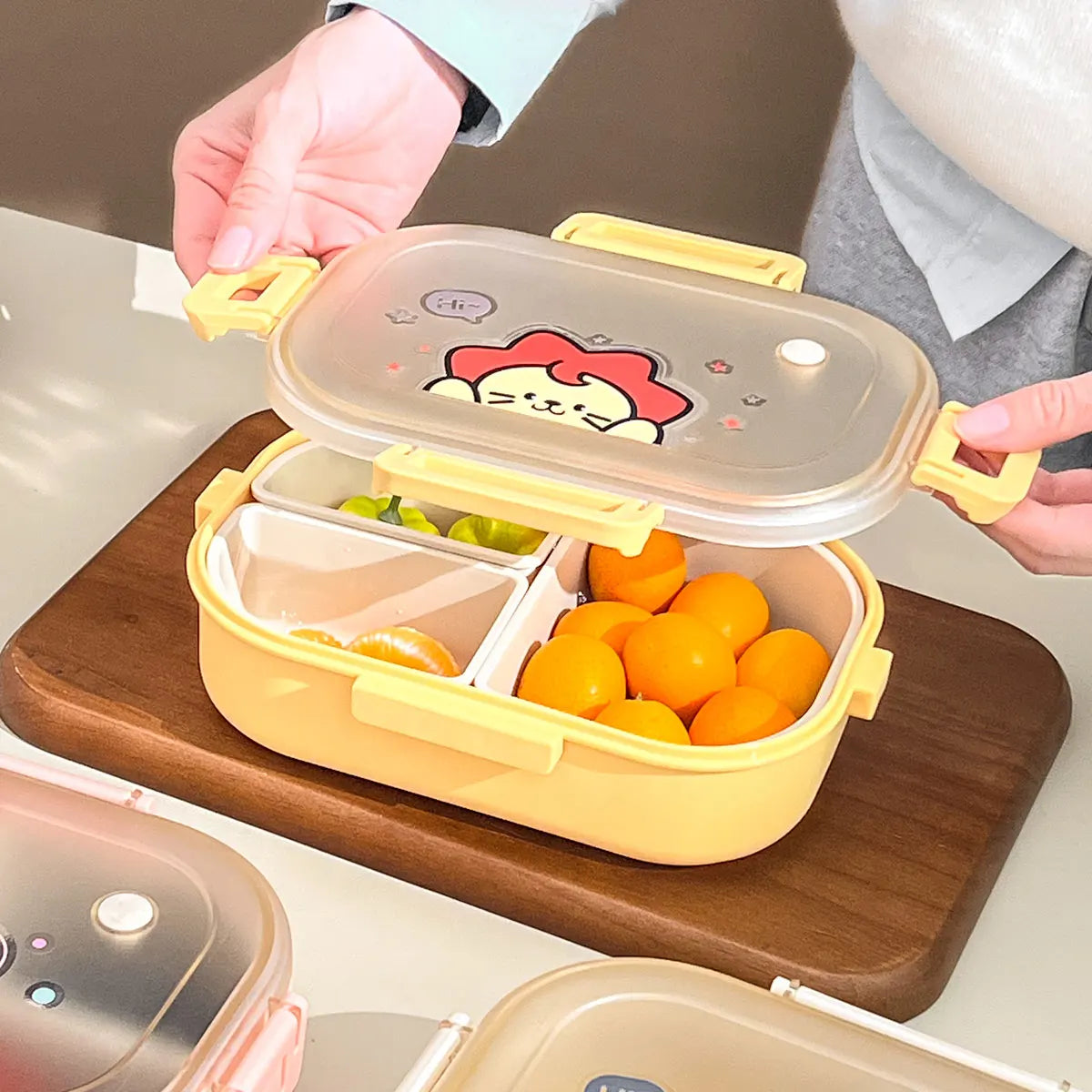 Yellow kawaii bento box with cartoon cat lid on a wooden cutting board