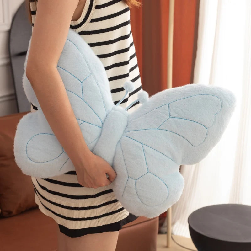 Person holding a large blue butterfly-shaped kawaii pillow indoors.