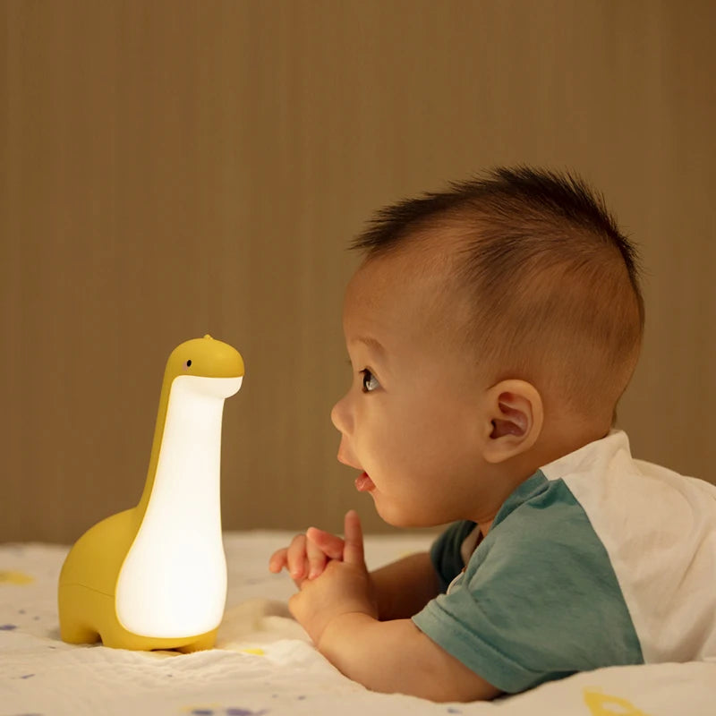 Baby looking at a dinosaur-shaped kawaii night light on a bed