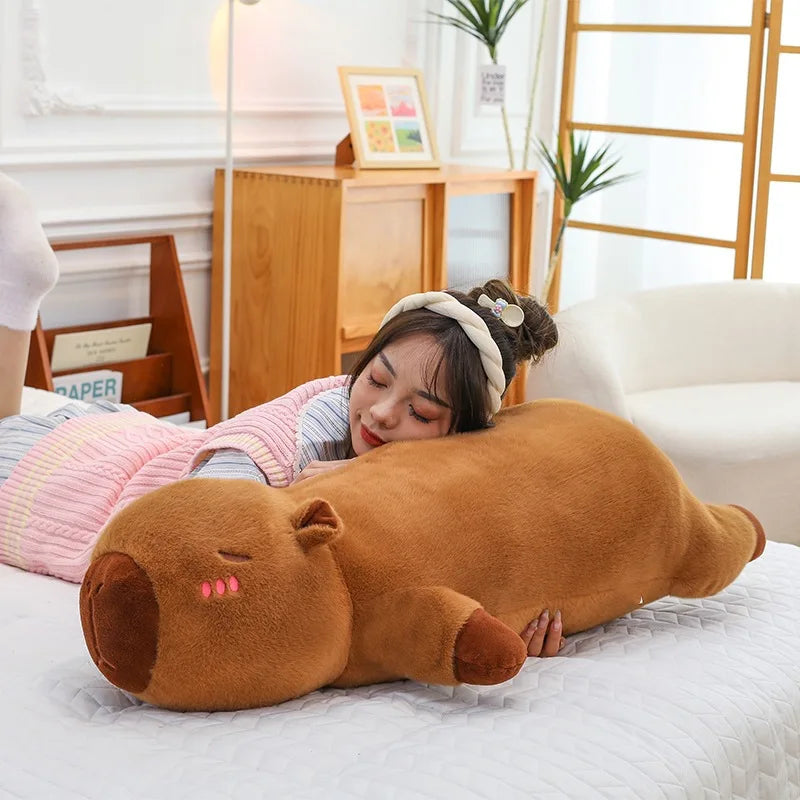 Person lying on a bed with a large brown animal-shaped kawaii pillow