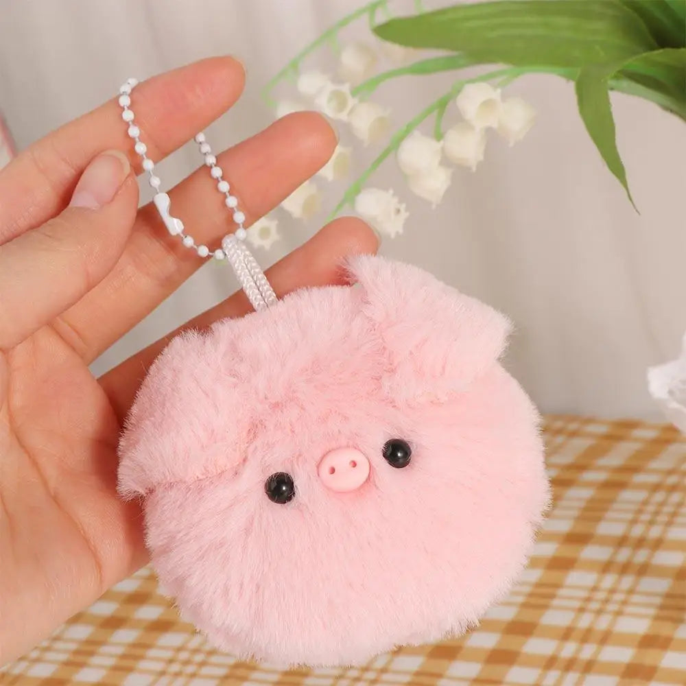 Pink kawaii fluffy keychain shaped like a pig held by a hand with a blurred background