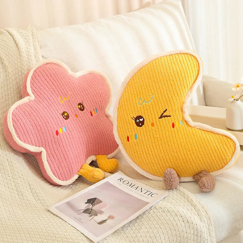 Two cute cloud-shaped kawaii cushions, one pink and one yellow, on a couch with a magazine underneath.