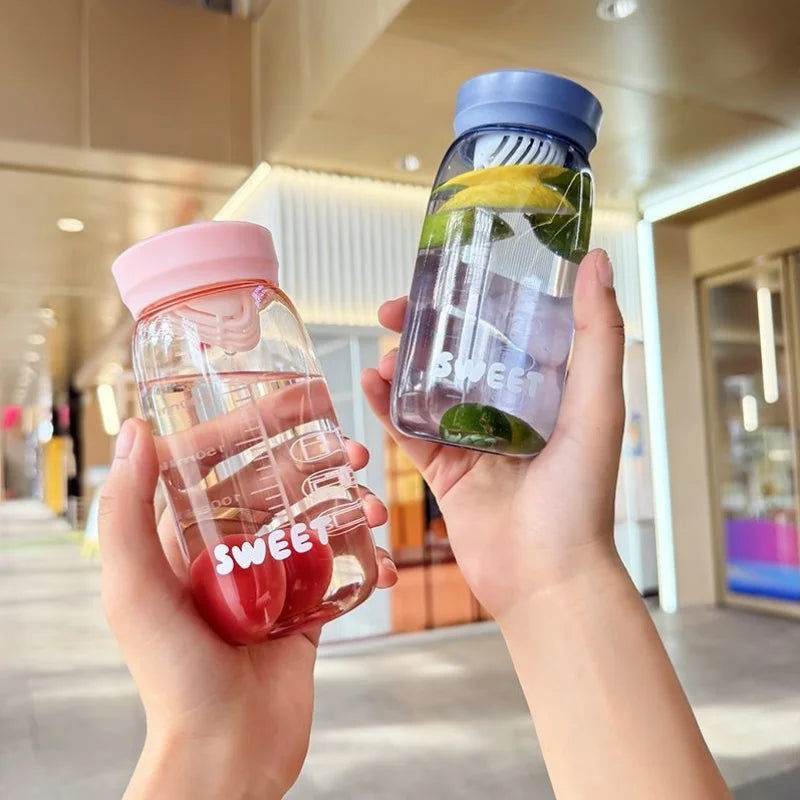 Two hands holding transparent water bottles with Kawaii colorful lids in an indoor setting.
