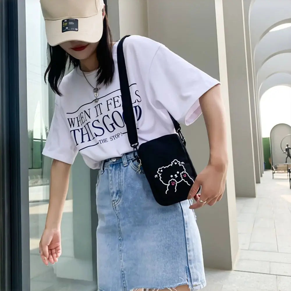 Person wearing a white t-shirt with text, blue denim skirt, and beige cap, holding a black Kawaii-style crossbody bag.