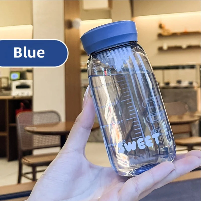 Clear Kawaii water bottle with blue lid held in a hand, blurred indoor background