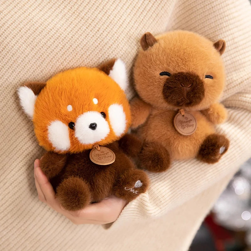 Two plush kawaii toys, one resembling a red panda and the other a bear, held in a hand against a beige background.