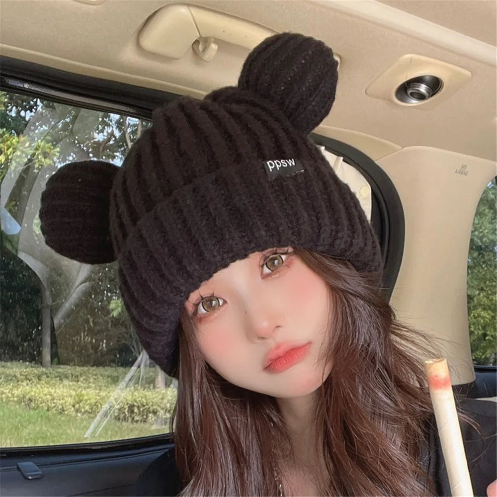 Person wearing a dark knitted Kawaii hat with pom-poms inside a vehicle.