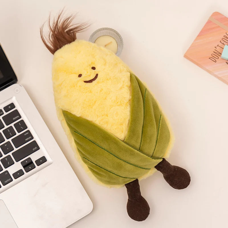 Plush kawaii toy shaped like a corn on the cob with a smiling face on a desk next to a laptop.