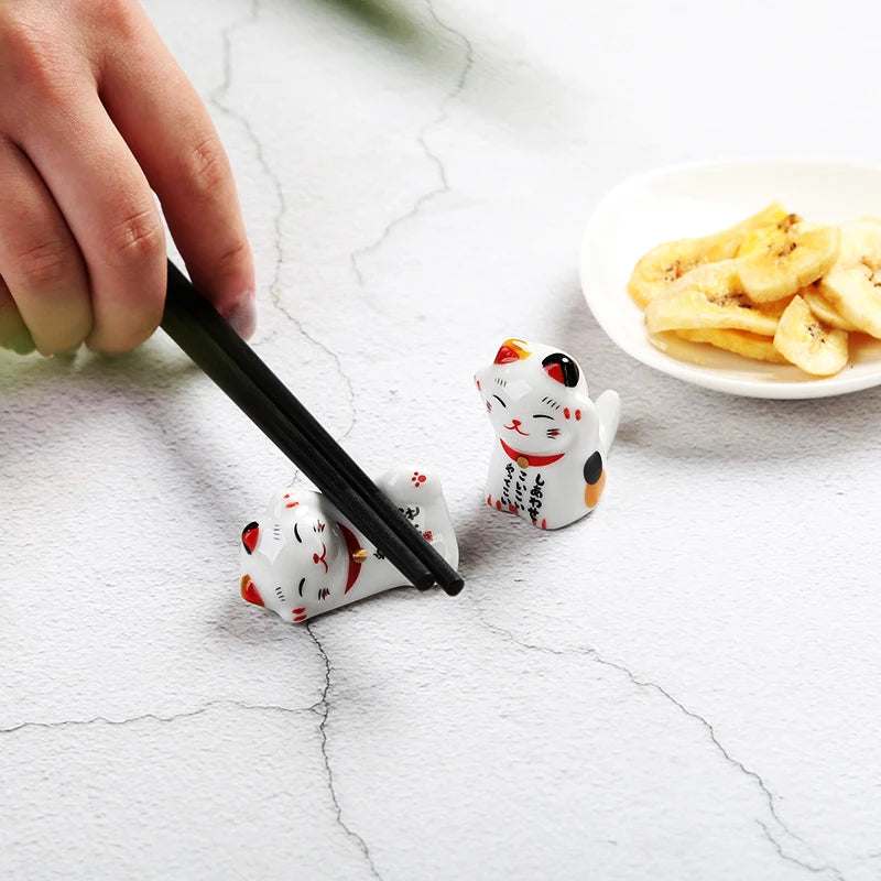 Kawaii figurines with chopsticks on a textured surface with a plate of food in the background.