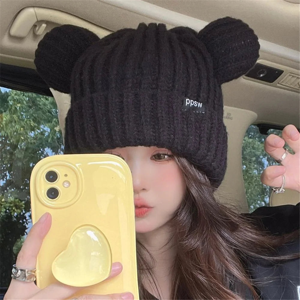Person wearing a black knit Kawaii hat with bear ears, holding a yellow phone case inside a vehicle.