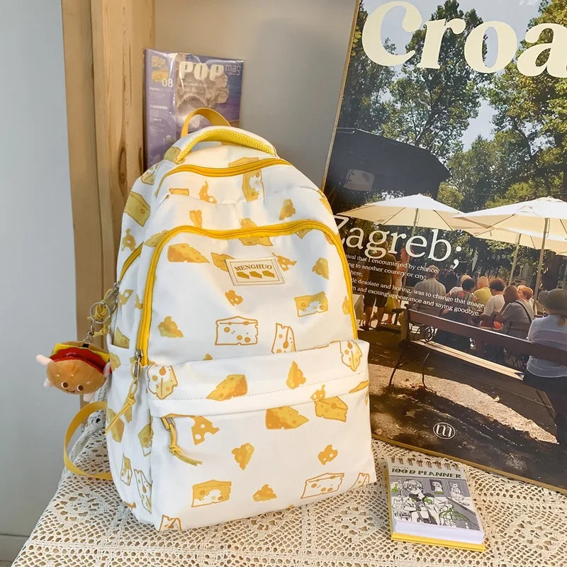 White backpack with Kawaii yellow patterns on a table with magazines and a notebook.
