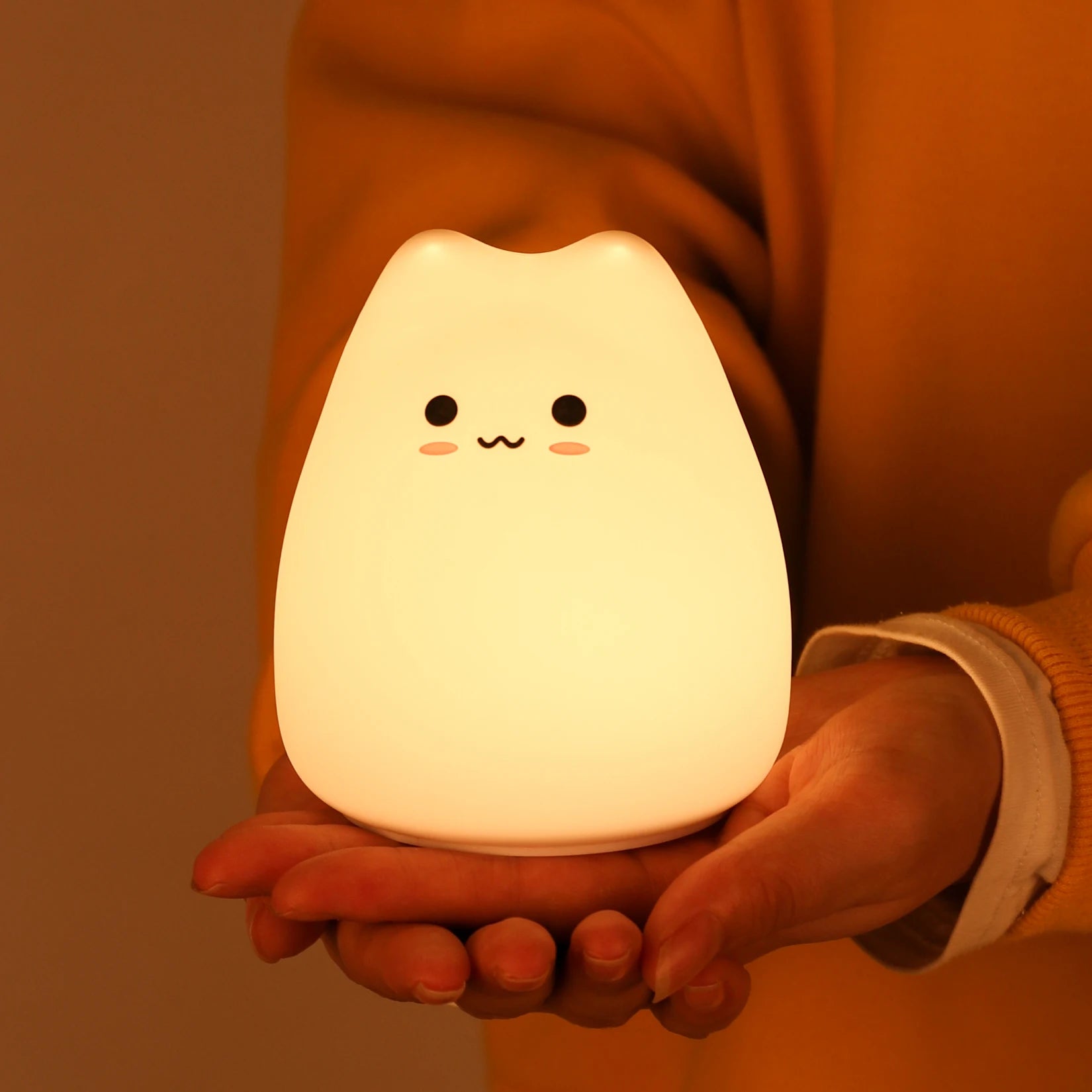 Person holding a kawaii cat-shaped night light with a warm glow against a brown background