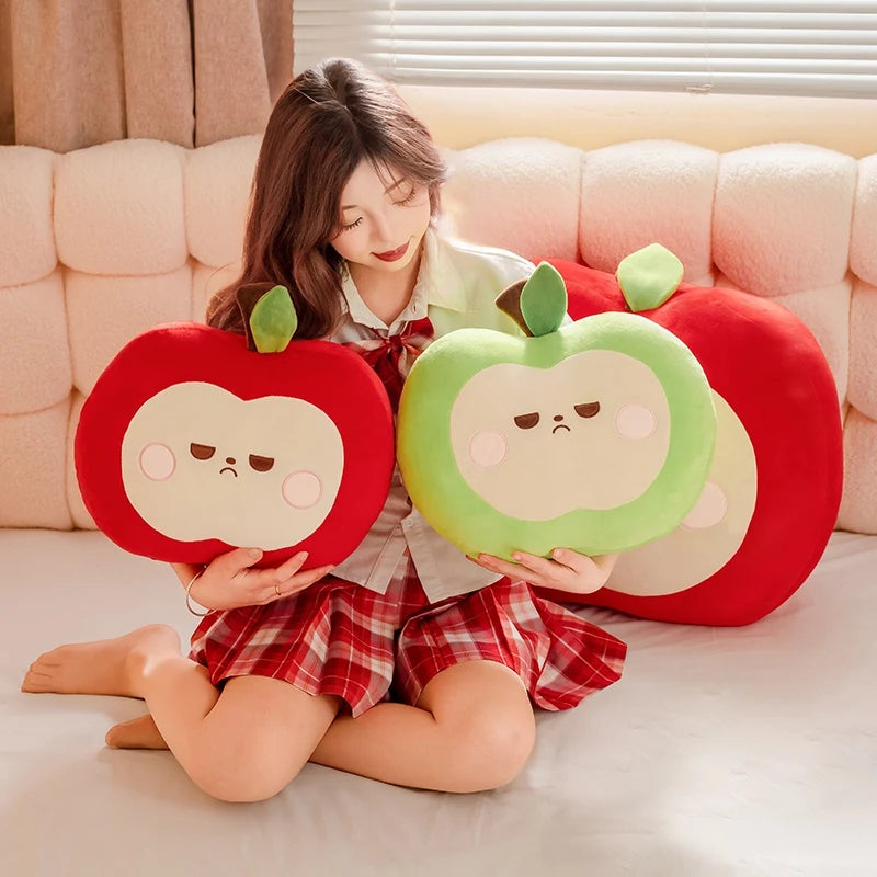 Person holding two red and green kawaii apple-shaped cushions on a couch.