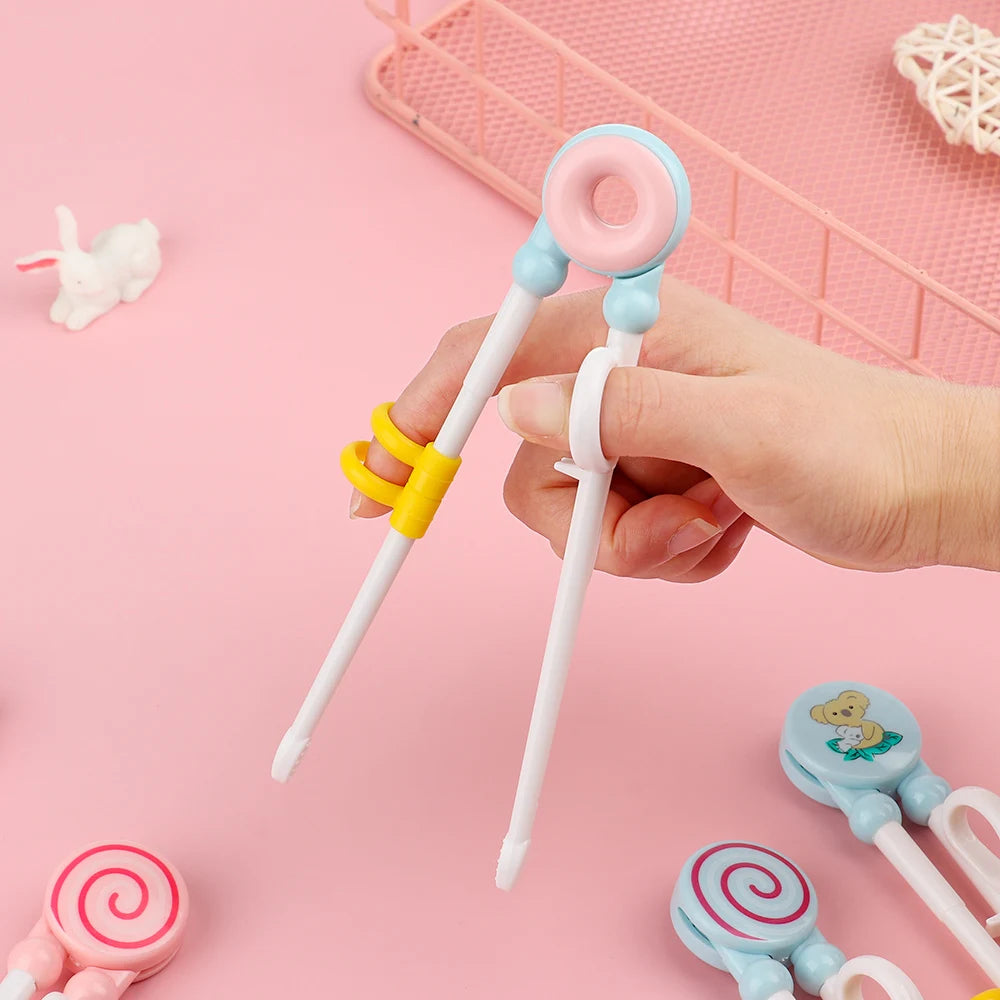 Hand holding a pair of colorful kawaii cartoon-themed chopsticks against a pink background