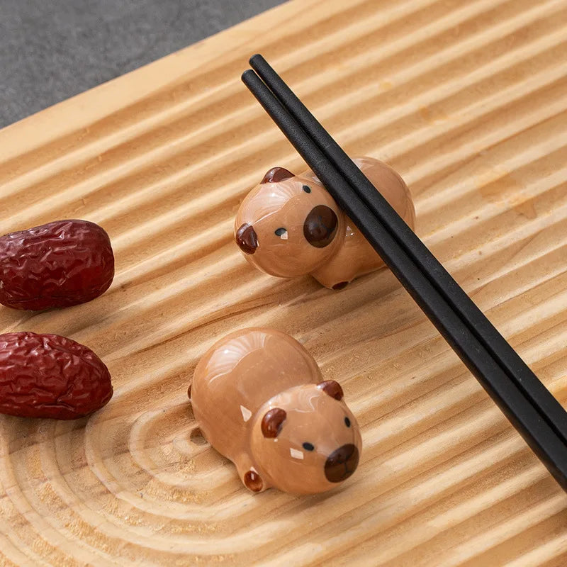 Two kawaii bear-shaped ceramic chopstick rests on a wooden surface with two red dates.