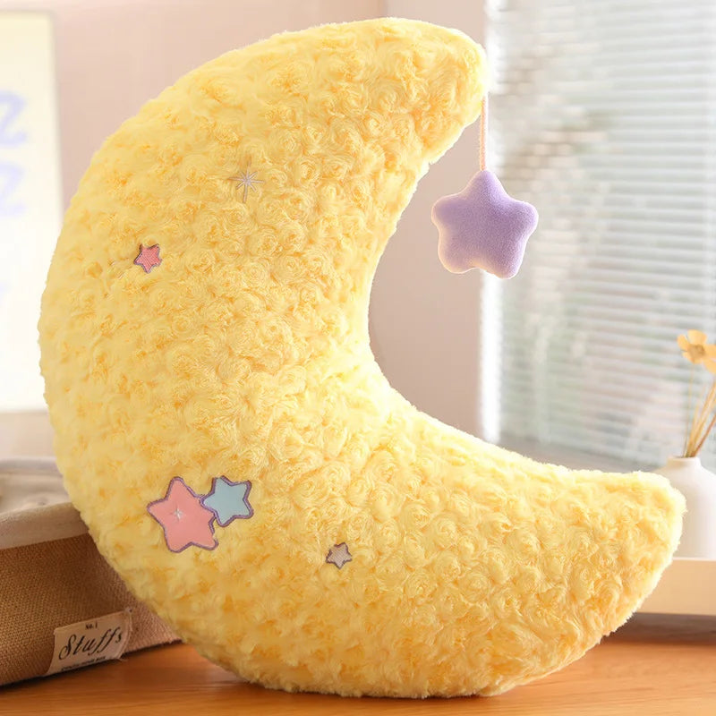 Yellow crescent moon-shaped kawaii pillow with star decorations on a wooden surface.