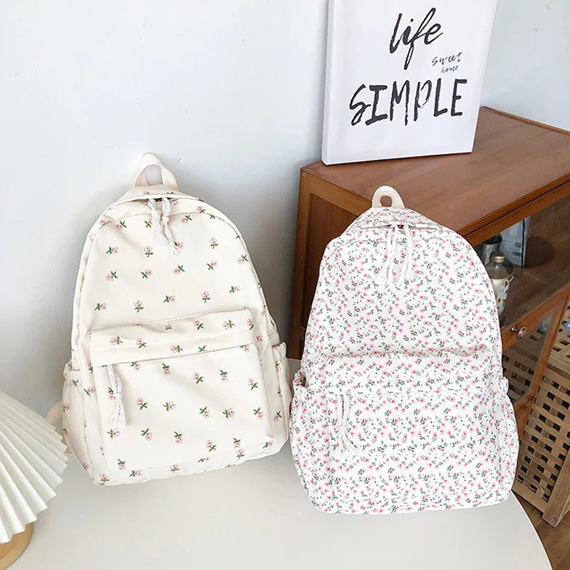 Two Kawaii floral-patterned backpacks on a light surface with a wooden shelf in the background.