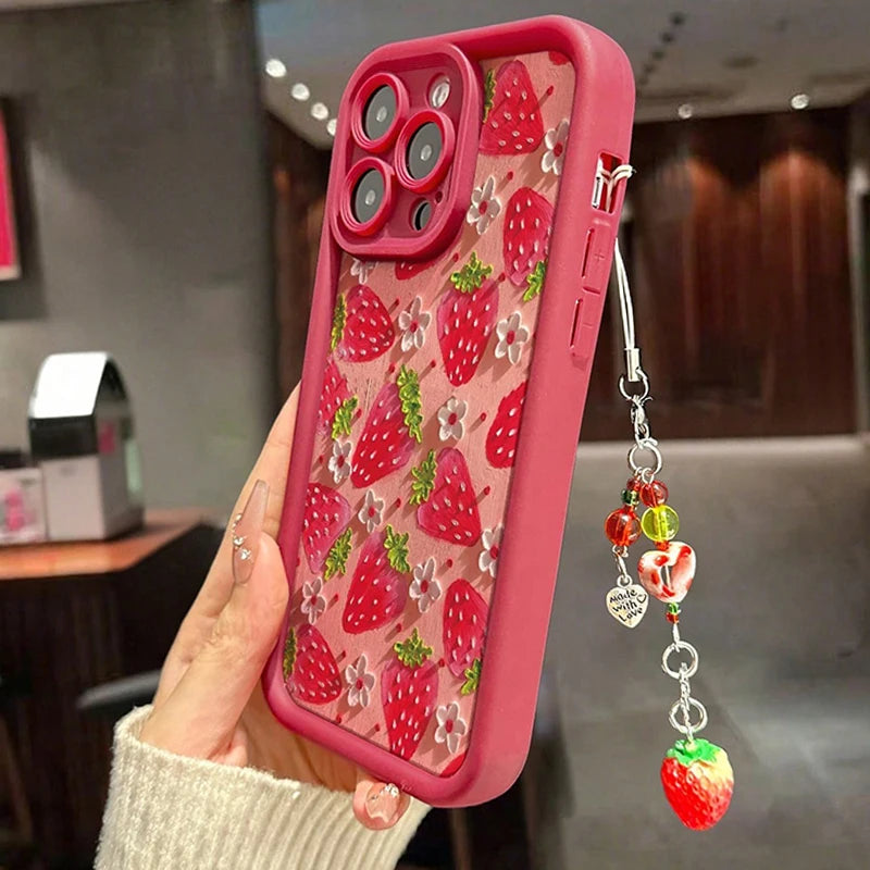 Phone case with kawaii strawberry pattern and charm held by a person indoors.
