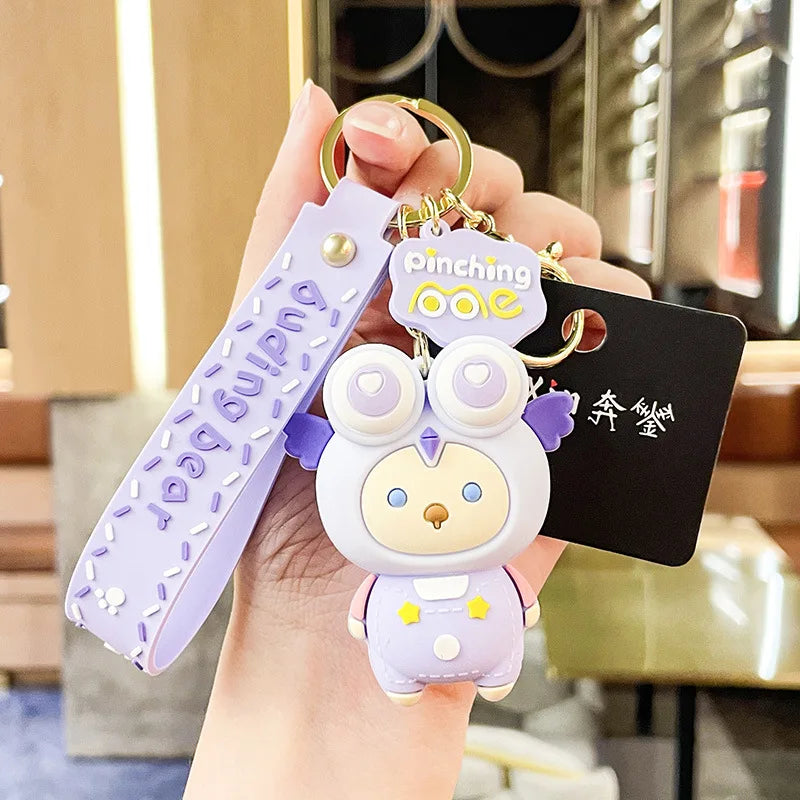 Keychain with kawaii cartoon character and text held by a hand against a blurred indoor background