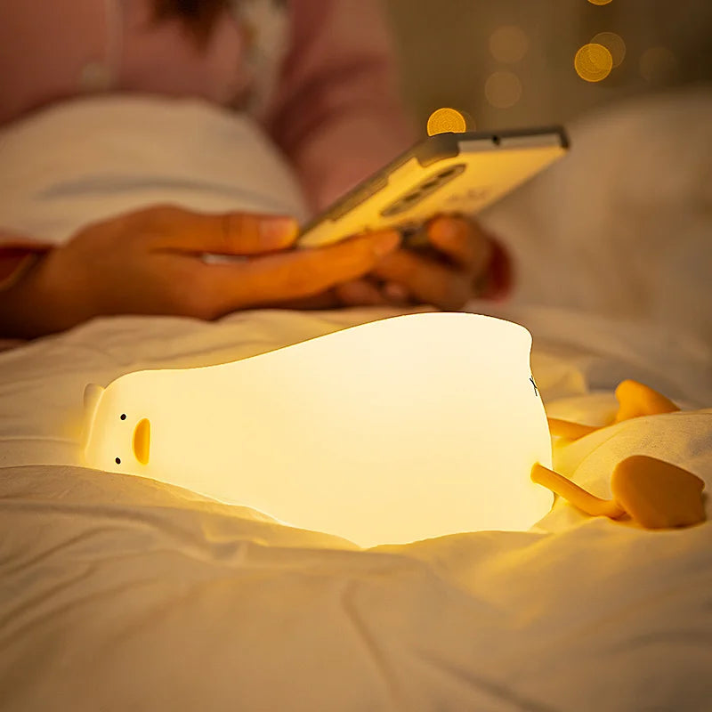 Person lying in bed using a smartphone with a glowing kawaii night light on the bed.