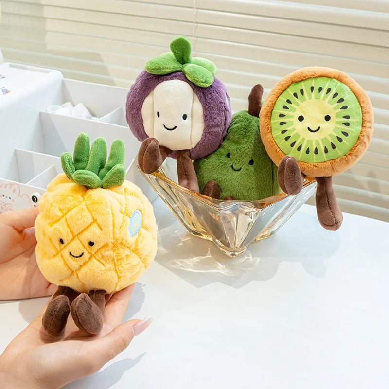 Plush kawaii toys shaped like a pineapple, avocado, and kiwi in a glass bowl on a white surface.