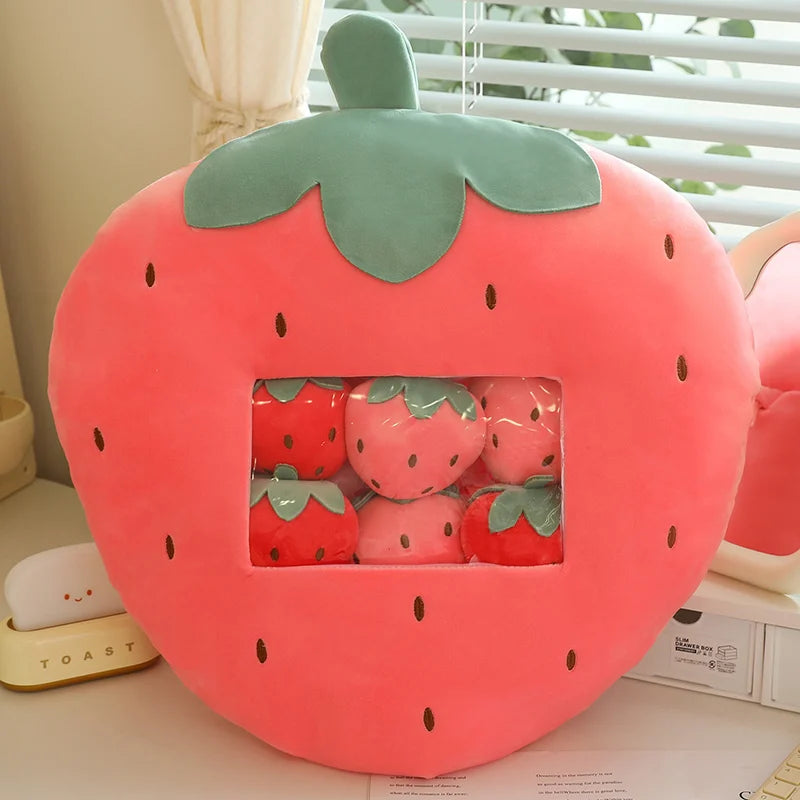 Strawberry-shaped kawaii cushion with small strawberry plush toys inside on a desk.