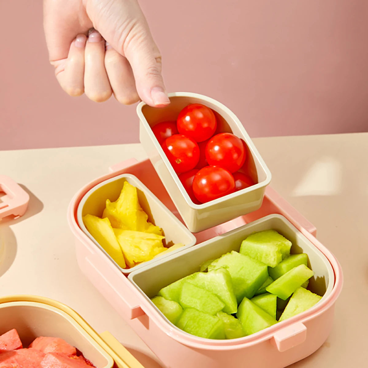 Pink kawaii bento box with compartments filled with fruits and vegetables on a pink background